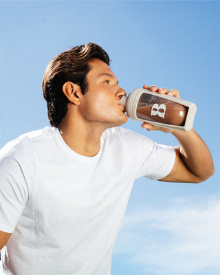 Man drinking from a bottle with a brand logo against a clear blue sky