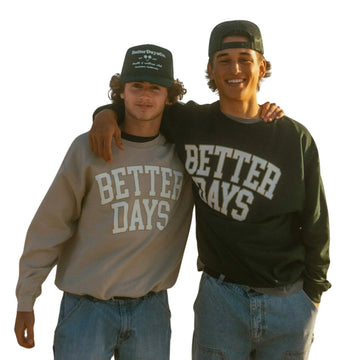 Two people in caps and jeans, one with arm around the other, wearing “BETTER DAYS” sweatshirts.