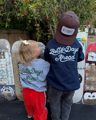 Two children wearing 'Better Days Ahead' shirts standing in front of skateboards.