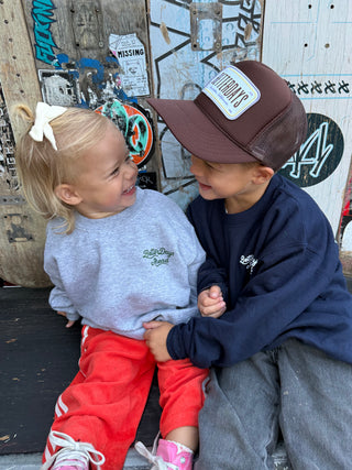 Two children sitting and holding hands in front of a wooden wall with graffiti.