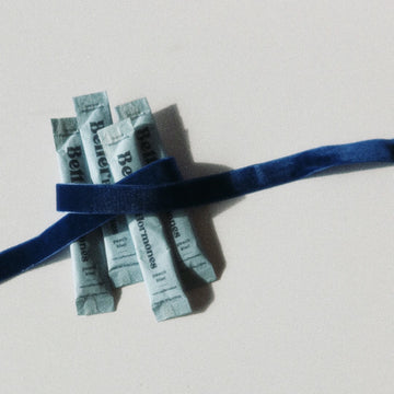 Four light blue packets tied with a dark blue ribbon on a light surface.