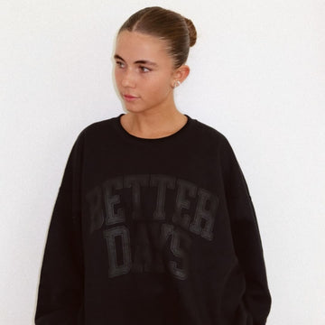 Young woman with hair in a bun wearing an oversized black sweatshirt, looking left against a plain background.