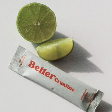 Lime half and wedge beside a sachet labeled “Bettercreatine” on a light surface with shadows