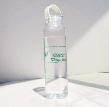 Clear water bottle with white loop cap, partly filled, with green “Better Days Co.” logo on front.