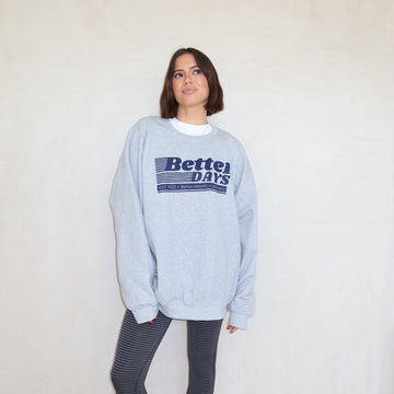 Woman in gray “Better Days” sweatshirt and striped leggings standing against a plain white wall.