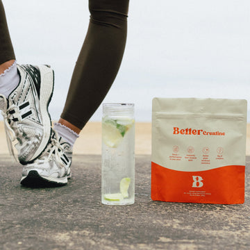 Runner’s legs in sneakers beside a water bottle with citrus and a BetterCreatine supplement pouch on pavement.
