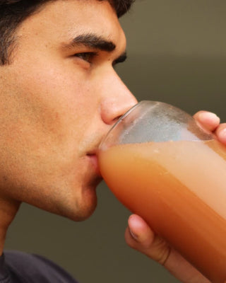 Man drinking from a glass of juice against a neutral background